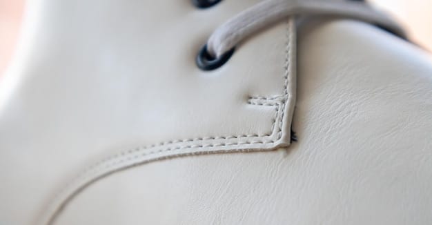 A close-up shot of a pair of elegant designer sneakers, featuring a subtle texture on the upper made from recycled plastic bottles. The background is a clean, bright studio setting highlighting the craftsmanship.