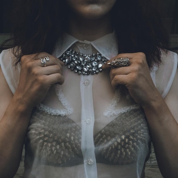A close-up of a hand delicately adjusting a multi-layered gold-tone statement necklace with intricate hammered metal details, worn over a simple black top, showcasing its bold yet elegant presence.
