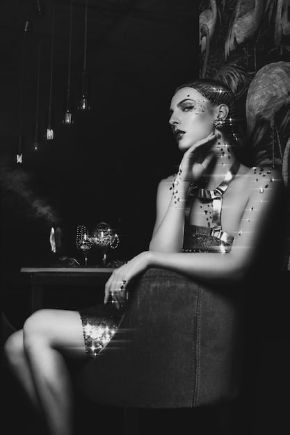 A woman in a black evening dress, wearing dramatic chandelier earrings and a bold cuff bracelet, laughing at a dimly lit restaurant.