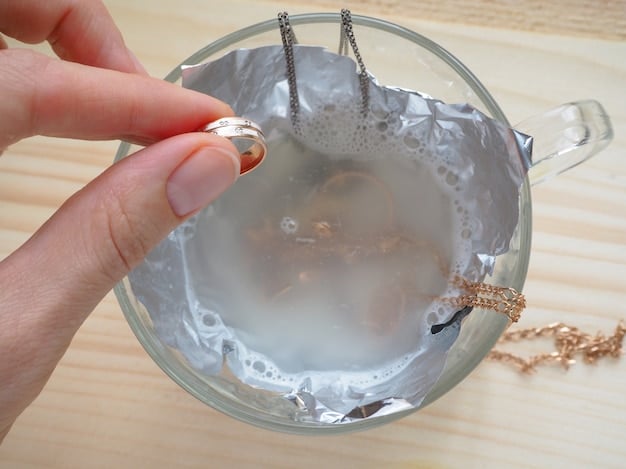 A person's hands gently cleaning a silver-plated fashion necklace with a soft brush and a bowl of soapy water, emphasizing careful handling.
