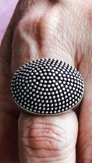 A detailed, clear view of an opened spring ring clasp with a small finger pressing its lever, showcasing its internal spring mechanism and circular design, against a muted, textile background.