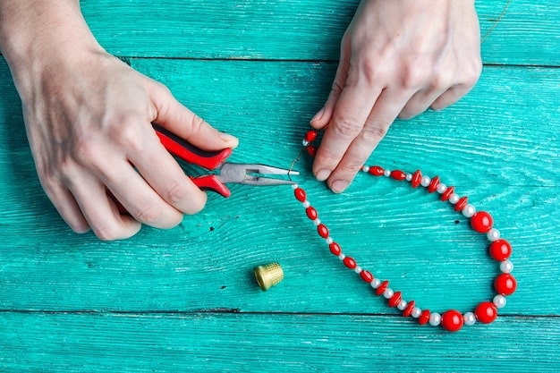 Hands meticulously putting together a necklace using small pliers, beads, and a chain, with a partially finished piece visible, showcasing the assembly process.