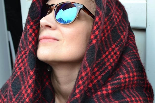 A close-up of a person's face wearing oversized, stylish UV-protective sunglasses and a light UPF scarf draped around their neck, with clear sunbeams in the background.