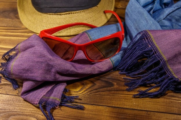 A detailed flat lay of various lightweight summer scarves in different prints and colors (e.g., silk, linen, cotton). Some accessories like sunglasses and a straw hat are artfully placed next to them.