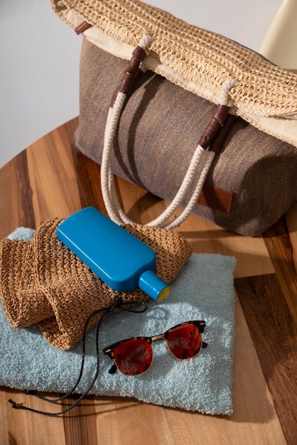 A close-up of a stylish straw tote bag on a beach, filled with sunglasses, a wide-brimmed hat, and a light scarf, conveying effortless daytime summer style.