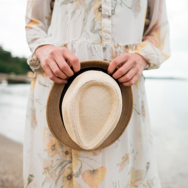 A close-up of a hand delicately adjusting a straw fedora hat, with a blurry background of a light-colored linen shirt, showcasing sophisticated summer accessories.