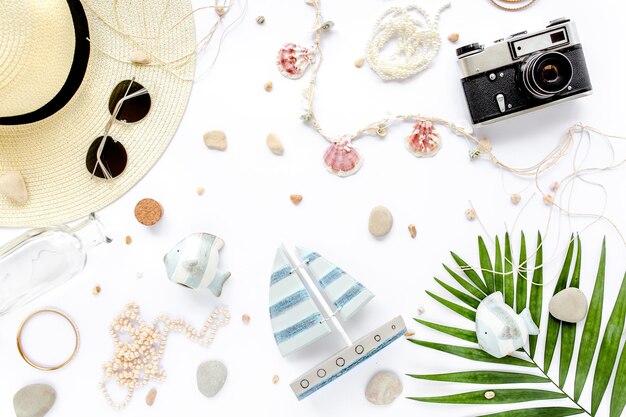 A flat lay of various summer accessories including a large resin bangle, a small handbag with polished gold hardware detail, and a beaded fruit-shaped clutch, all artfully arranged on a light-colored linen fabric with some scattered seashells, conveying a sense of curated summer style.